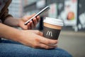 Minsk, Belarus, July 02, 2019: Hands holding paper cup with McDonald`s logo and uses a smartphone