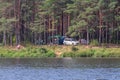 Tourists camped in the woods on the river bank: tents, awnings, and a car. A man catches