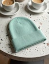 Mint Green Knitted Beanie on Speckled Table with Two Cups of Coffee Royalty Free Stock Photo