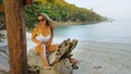 The sexy vibrant young lady is posing on a tree. The woman is having fun on an island vacation. The licentious woman