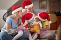 Mionor sisters looking at baby brother, sitting in laps of young parents, wearing santa hats