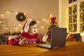 Shocked child sitting at table with laptop looking at real Santa Claus on video chat