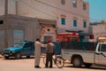 Mirleft, Morocco - adult man covers face with left hand, taps right on male friend\'s shoulder. Animated conversation.