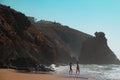 Mirleft, Morocco - two white females in bikinis walk towards the waves. Rugged cliffs, rock formations in Aftas Beach. Royalty Free Stock Photo