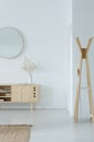 Mirror above stylish wooden cupboard with glass vase and flower on it, modern clothes hanger in the corner of white hall Royalty Free Stock Photo