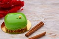 Glaze mousse gren cake with cinnamon sticks over white wooden background witg red dry flowers