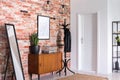 Mirror next to wooden cabinet in entrance hall interior with white door and poster on red brick wall Royalty Free Stock Photo