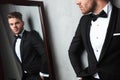Mirror reflection of relaxed young man wearing a black tuxedo