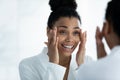 Mirror reflection smiling African American woman doing facial massage