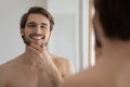 Smiling young 30s handsome well-groomed man looking in mirror. Royalty Free Stock Photo