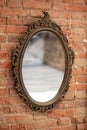 A mirror in a vintage openwork frame hangs on an old brick wall