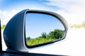 Mirror wing of white car with reflection of green trees blur in mirror. Royalty Free Stock Photo