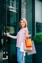 Positive woman near entrance to the shop holding paper bags