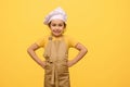 Mischievous child girl dressed as confectioner in apron and white chef's cap, putting hands on waist, looking at Royalty Free Stock Photo