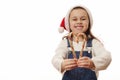 Mischievous adorable little child girl, wearing Santa hat, holding red and green strippes candy canes in shape of heart Royalty Free Stock Photo