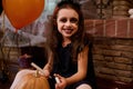 Mischievous little girl witch, with a spider on her face, smiles looking at camera, drawing a scary face on a pumpkin Royalty Free Stock Photo