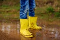 Mischievous preschooler child wearing yellow rain boots jumping in large wet mud puddle. Kid playing and having fun. Outdoors Royalty Free Stock Photo