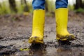 Mischievous preschooler child wearing yellow rain boots jumping in large wet mud puddle. Kid playing and having fun. Outdoors Royalty Free Stock Photo