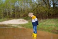 Mischievous preschooler child wearing yellow rain boots jumping in large wet mud puddle after rain. Kid playing and having fun.