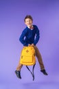Mischievous schoolboy in uniform with backpack jumps on purple background