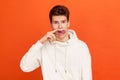 Mischievous teenager in white casual style hoodie putting finger into his nose and showing tongue, fooling around, bad habits,