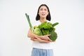 Miserable asian woman, holds green vegetables and complains at het diet, looks at calories, white background