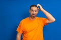 Miserable and gloomy guy with messy hair, frowning and looking unsatisfied while scratching head, standing over blue Royalty Free Stock Photo