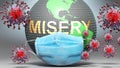 Misery and covid - Earth globe protected with a blue mask against attacking corona viruses to show the relation between Misery and