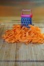 Mismatch: a large carrot next to a small grater. Cutting board on the kitchen table.