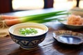 miso paste beside bowl of soup, green onions garnish