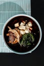 Miso soup classic with beef on blue pastel color plate at black background with sunlight and shadows, minimalism,top view