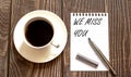 WE MISS YOU - white paper with pen and coffee on wooden background Royalty Free Stock Photo