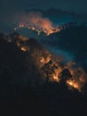 Mist envelopes a hilly forest as firelight glows through the trees, creating a hauntingly beautiful landscape at night. Royalty Free Stock Photo