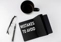 MISTAKES TO AVOID written text in small black notebook with coffee , pen and glasess on white background. Black-white style