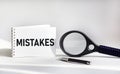 MISTAKES- word on notepad and white background, pen, magnifier near. Business concept: buy, sell, commerce. Copy space Royalty Free Stock Photo