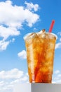 Misted disposable plastic cup with iced tea and straw stands on base against blue sky Royalty Free Stock Photo