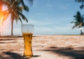 Misted glass of cold beer on the sand at the background of green palm trees, blue sky and sea coast. Tropical island. Royalty Free Stock Photo