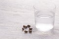 Misted glass of water and brown medical capsules on a white old wooden table