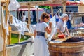 Mistress checking maid washing linen, servant woman in old traditional clothes near wooden barrel in historical centre