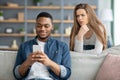 Mistrust. Attentive Lady Looking At Black Boyfriend While He Texting On Smarthone