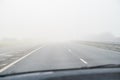 A misty, foggy road and dashed white centre line as seen through a car windscreen. There is slight motion blur