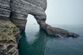 Misty morning fog at the rocky beach. Chalk cliff arch in Etretat in Normandy