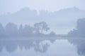 misty morning by the lake with calm water, fog and reflections of trees in mirror Royalty Free Stock Photo
