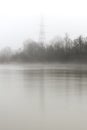 Misty river bank and electrical tower on a foggy morning, monochromatic scene Royalty Free Stock Photo