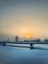 Misty sunrise over the field with wooden fence and village Royalty Free Stock Photo