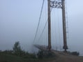 Misty suspension bridge fog view. Altai village bridge. Early misty morning Royalty Free Stock Photo