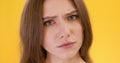 Close up portrait of young puzzled lady shaking head no and looking at camera with question, orange studio background