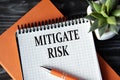MITIGATE RISK - words in white notebook on dark wooden background with cactus and pen