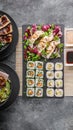 Mix of Asian dishes. Vegetable sushi maki rolls, gyoza dumplings with salad on a black stone board, pork and chicken dishes in Royalty Free Stock Photo