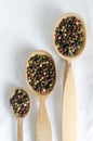 A mix of black, white, red and fragrant peppercorns in three wooden spoons on a light background. dried spice peppercorn concept Royalty Free Stock Photo